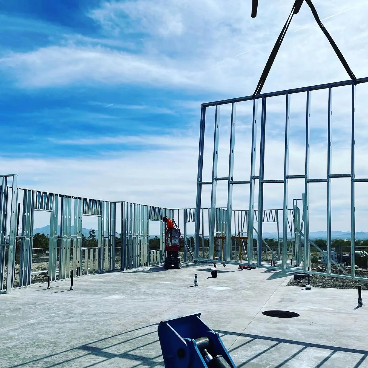 Steel wall panel being set by crane while a worker frames on a lift