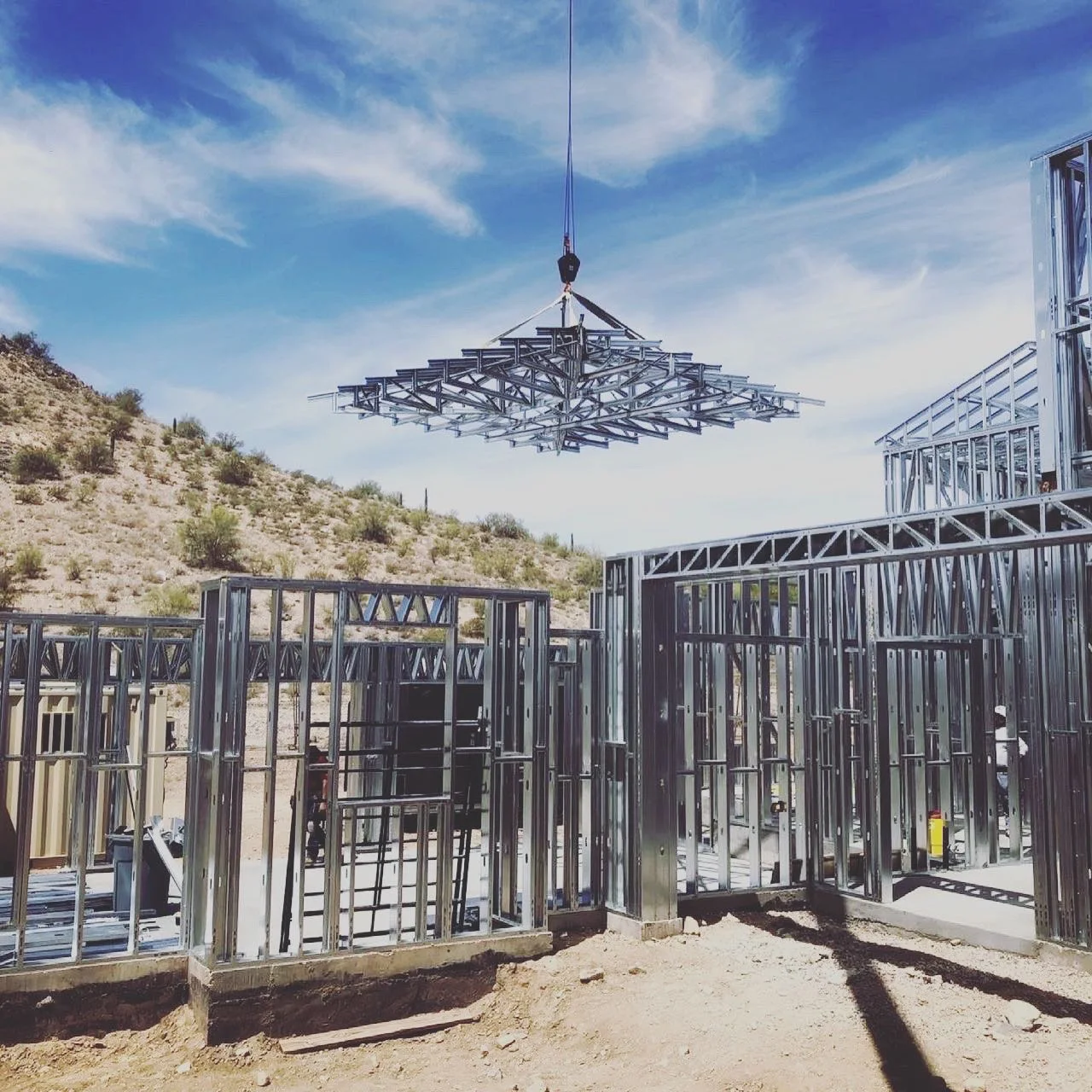 Steel roof trusses lifted by crane over steel-framed walls